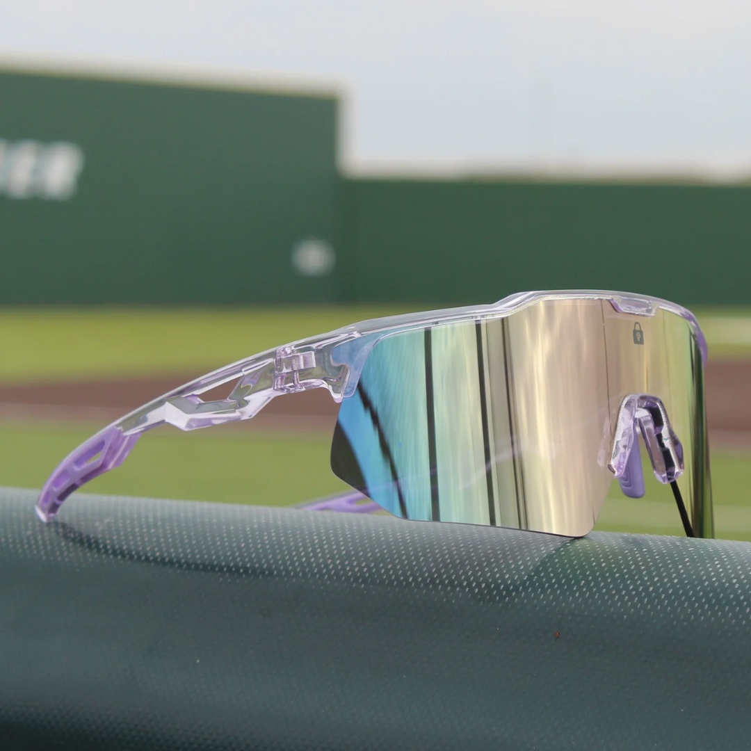 Size zoom view of PA10 Polarized Baseball Sunglasses with a vibrant purple reflective mirror lens and pink clear frame, resting on the dugout railing with a baseball field in the background, ready for action.