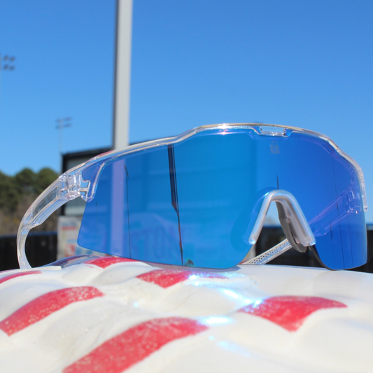 Clear frame sports sunglasses with blue mirrored lens from Locked Eyewear, resting on a white and red baseball glove under a clear blue sky.