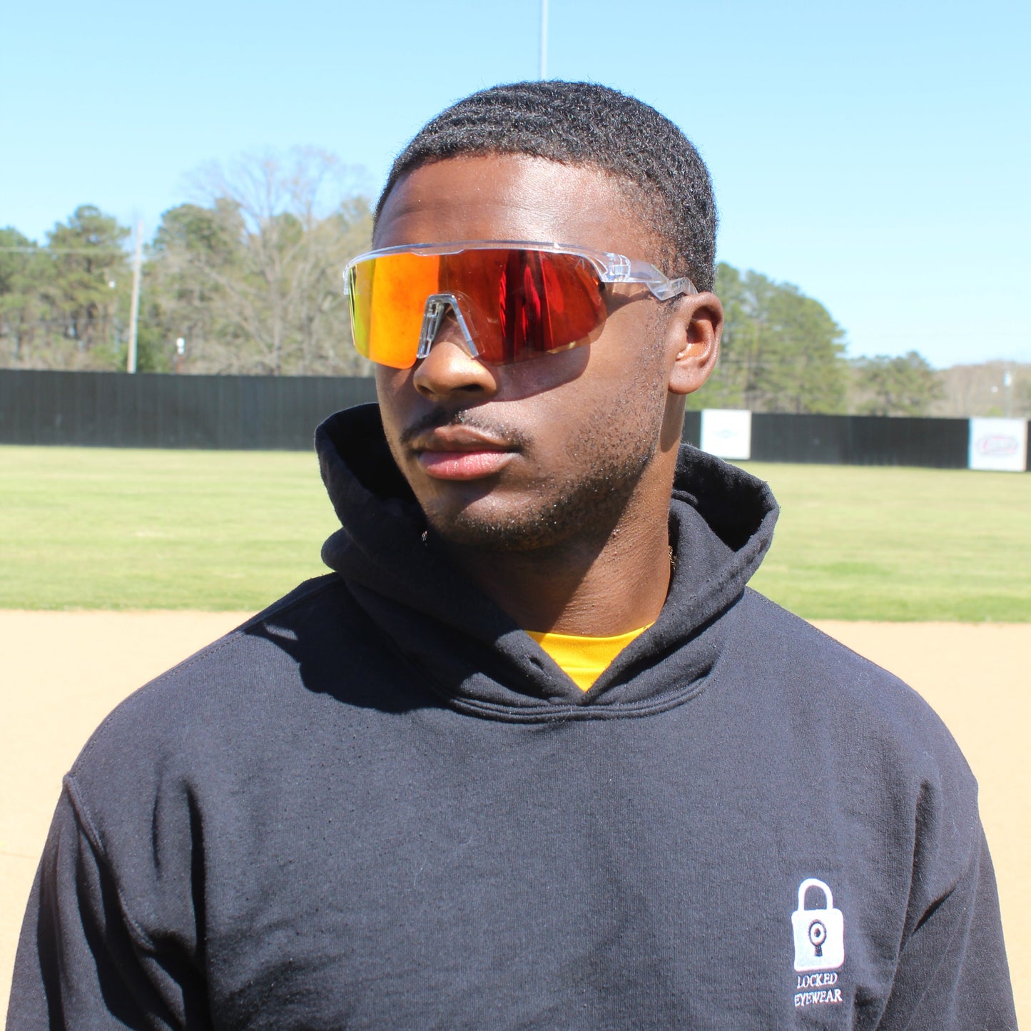 Locked Eyewear Revelation red lens baseball sunglasses worn by a hitter in the batter’s box during a game, the high-contrast non-polarized lens sharpening depth perception to pick up the pitch